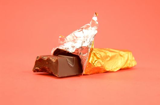 A half eaten chocolate bar in the wrapper.  Reddish pink background