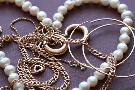 Closeup of various gold and pearl jewelry on brown textiles background