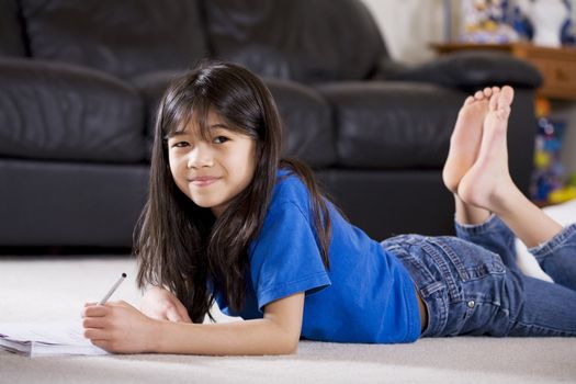 Little girl doing her homework lying on floor