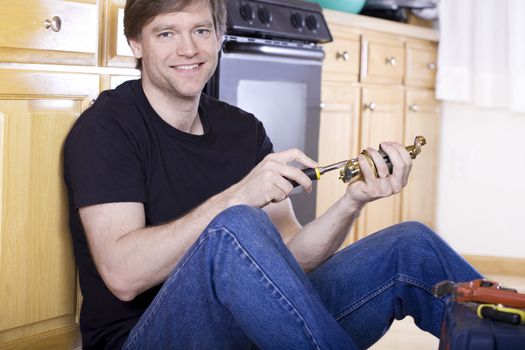 Handsome man in thirties sitting on kitchen floor doing repairs