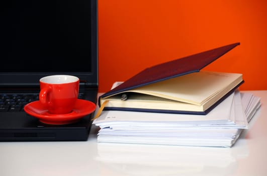 red cup over black notebook on office desk still life