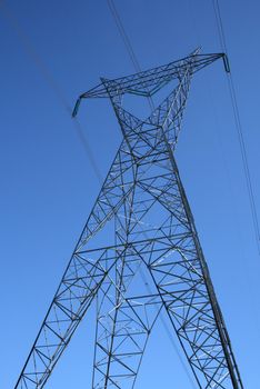 Silhouette of a high voltage electricity pylon against the deep blue sky.