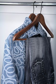 Blue jeans and shirts on wooden hangers in a closet.