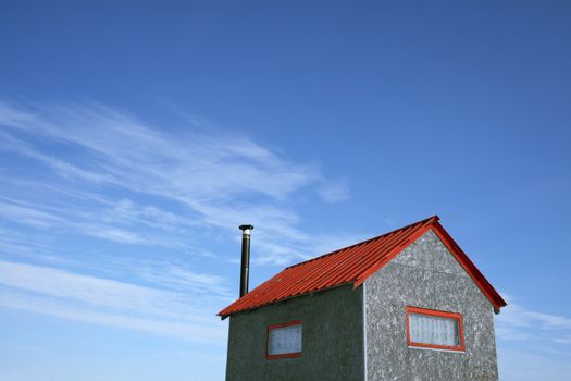 Little house with red roof and chimney and spacious blue sky (ice fishing hut).