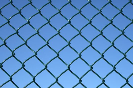 Green chain link fence on a blue sky background.