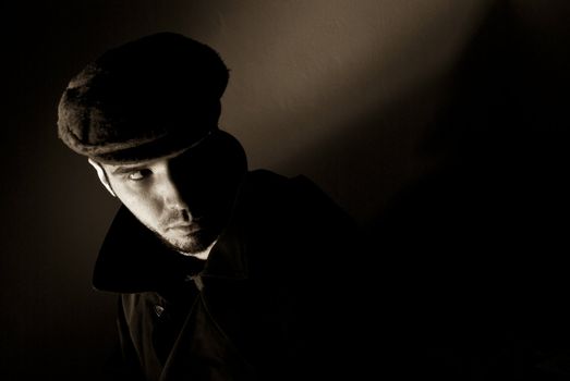 Sepia toned noir portrait of suspicious looking young man. Harsh highlights and shadows.