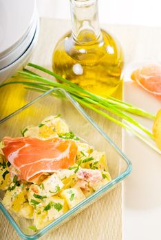 fresh home made parma ham and potato salad,with raw ingredients around with bowls and dishware on a table