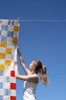 Young woman touching a bright patchwork counterpane hanging to dry on a clothes-line.