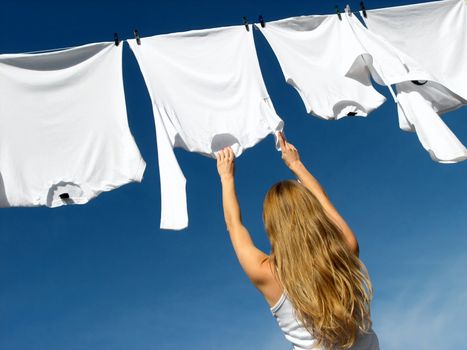 Longhaired young woman reaching white laundry which hangs to dry in a summer breeze on a clothes-line.