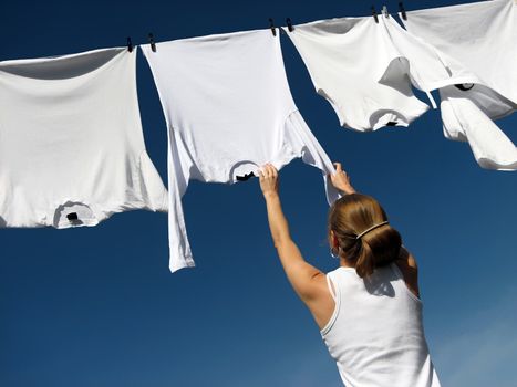 Young woman reaching white laundry which hangs to dry in a summer breeze on a clothes-line.