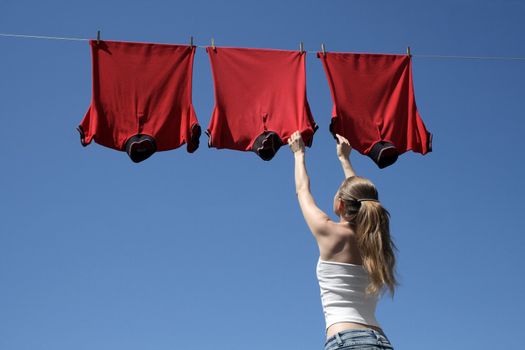 Young woman reaching red corporate t-shirts which hang to dry in a summer breeze on a clothes-line.