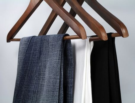 Blue jeans and trousers on wooden hangers.
