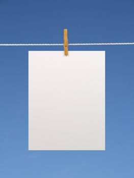 Blank paper sheet on a clothes line against the blue sky. Contains two clipping paths: 1) paper, clothes line and clothespin; 2) paper only