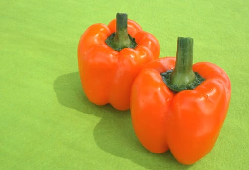 Two fresh orange peppers on green background.