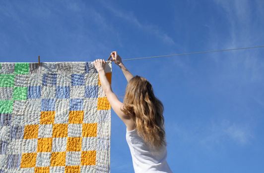 Longhaired young woman putting a bright counterpane on a clothes-line to dry in a breeze.