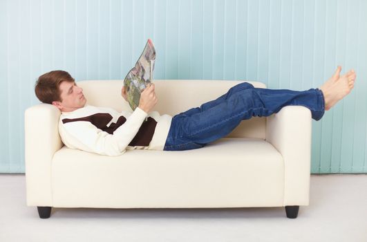 A young woman lies comfortably on a sofa with a magazine