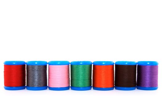 Row of colorful thread spools, on white background, with copy space.