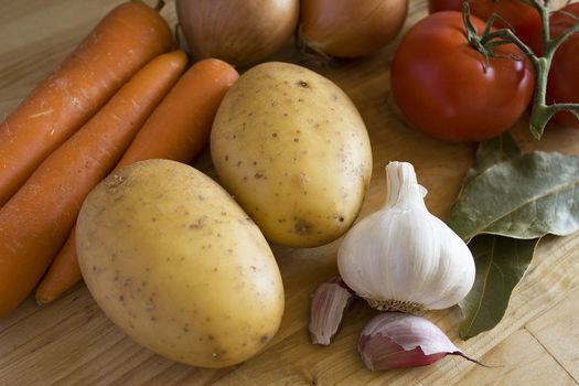 Some carrots, potatoes, onions, tomatoes, garlic and laurel on chopping board.