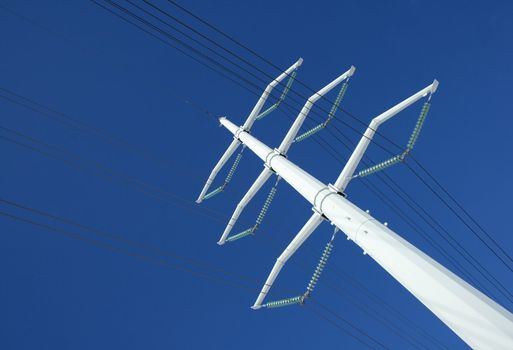 White high voltage electricity pylon and power lines against the deep blue sky.