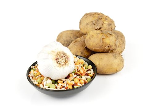 Small pile of brown unpeeled potatoes with soup pulses and garlic on a reflective white background