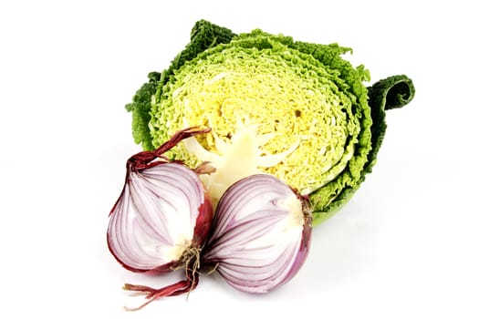 Raw red onion cut in half with half a green raw cabbage on a reflective white background