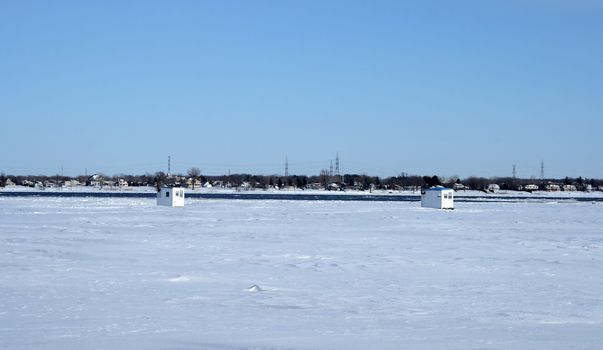 Winter landscape. Ice fishing huts on a frozen river.