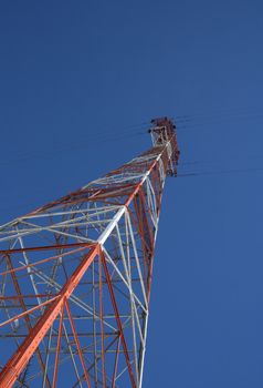 Red and white high voltage power tower in the blue sky.