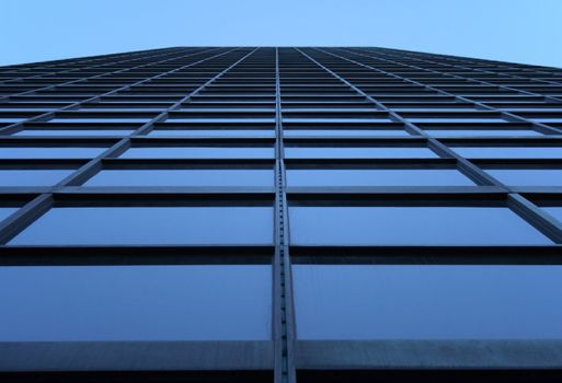 Glass-windowed skyscraper reaching the sky. View directly from below.