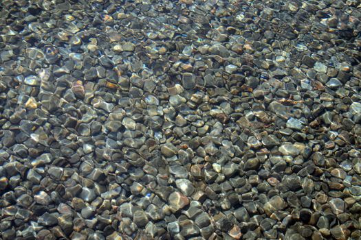 Bottom of a pond covered with stones seen through transparent water.