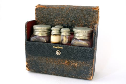 A vintage, distressed leather pharmaceutical case with a red lining, filled with two large bottles and three small vials.  One of the vials has a blank label facing forwards.