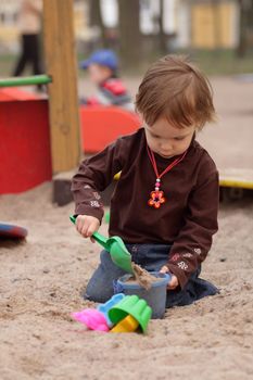 little beauty girl playing at sand-box. She with enthusiasm model of sand. 