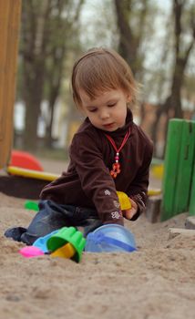 Little beauty girl playing at sand-box. She with enthusiasm model of sand. 