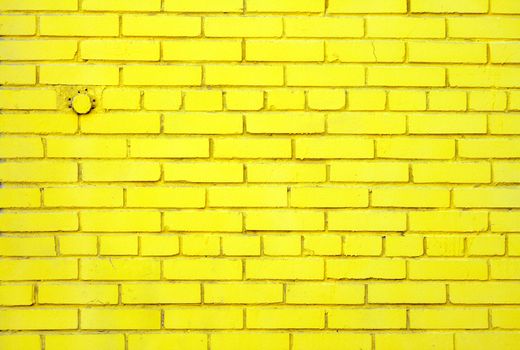 Slightly dusty old brick wall coloured yellow with embedded round closed pipe.