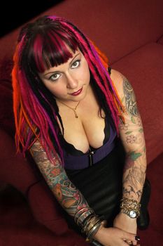 Portrait of a beautiful female goth with dreadlocks on a red couch.
