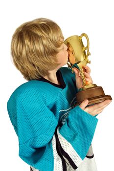 Young boy athlete kissing the championship trophy.  Face is visible in the reflection on the cup.
