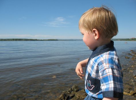 Small boy looks at the waters of river in solar summer day
