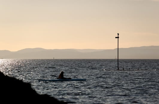 A cayack rower, resting by a marker pole. The image is set in the evening light in Oslo Fjord, Norway.
