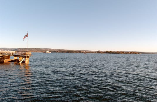 The waters of Oslo fjord with a pier and Norwegian flag in the foreground
