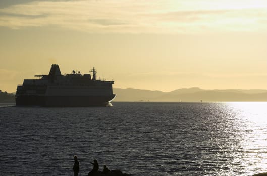 A high-contrast image of a departing ferry, sailing into the soft evening sunlight
