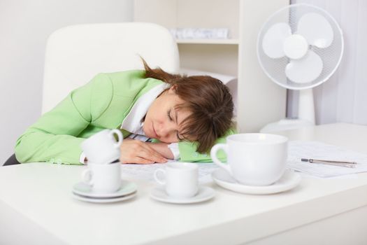 Tired woman sleeping on the desk in the office among the coffee cups