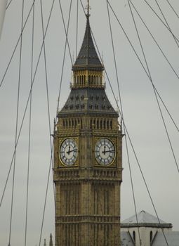 Clock of Big Ben seen through the spokes of the London Eye against a grey sky