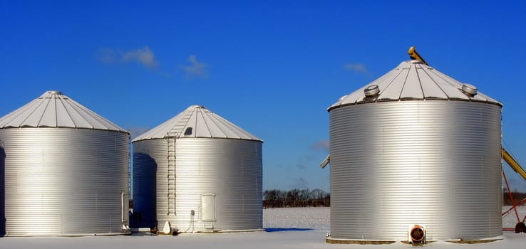 Three silos on a farm, under a vibrant blue sky