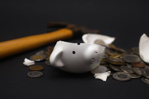 A broken piggy bank isolated on a dark background with loads of coins from around the world and a hammer.