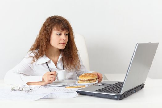 The girl, sitting in the workplace is going to eat a hamburger