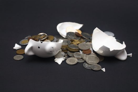 A broken piggy bank isolated on a dark background with loads of coins from around the world.