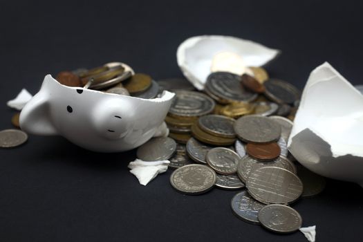 A broken piggy bank isolated on a dark background with loads of coins from around the world.