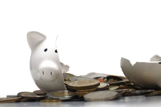 A broken piggy bank isolated on a white background with loads of coins from around the world.