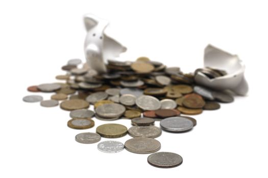 A broken piggy bank isolated on a white background with loads of coins from around the world.