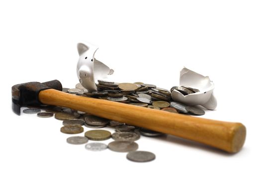 A broken piggy bank isolated on a white background with loads of coins from around the world and a hammer.