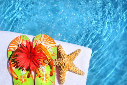 Colorful sandals with flower and white towel by the pool